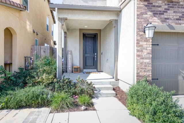 property entrance with a garage, brick siding, fence, and stucco siding