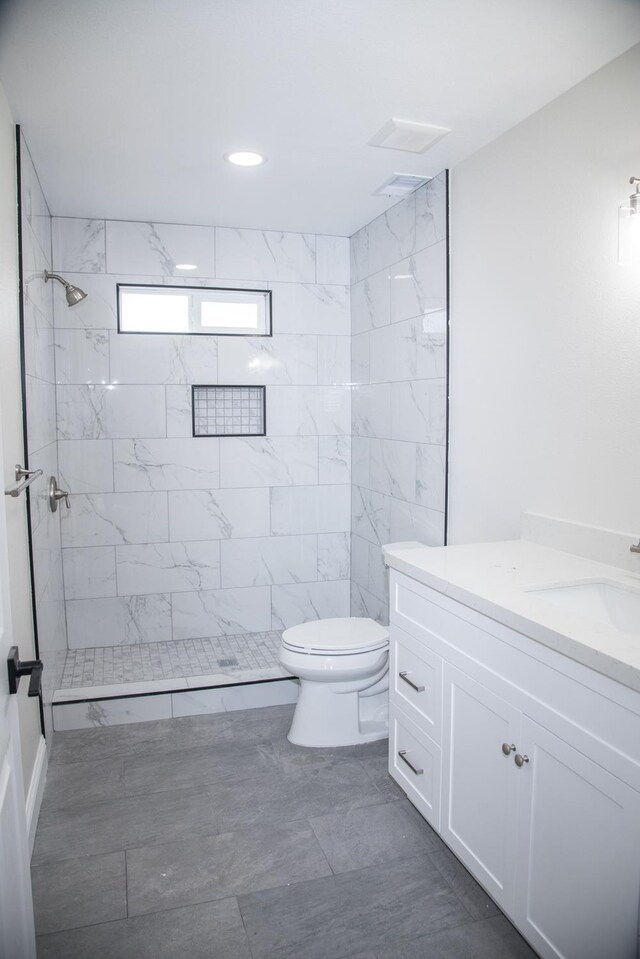 bathroom featuring toilet, a tile shower, and vanity