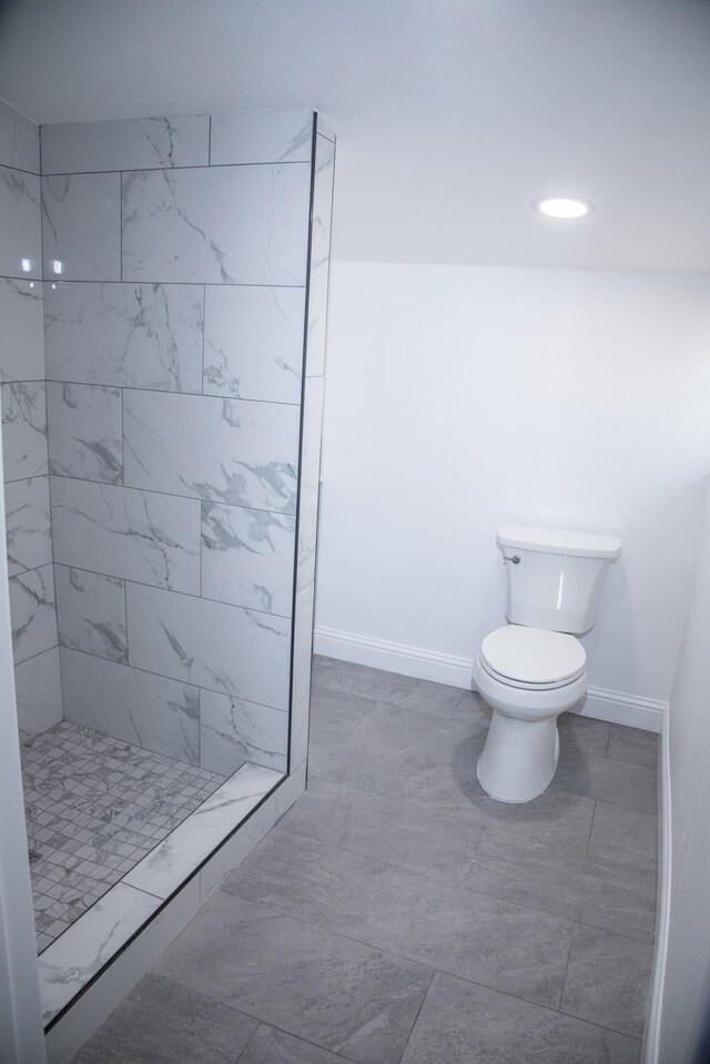 full bath featuring toilet, baseboards, and tiled shower