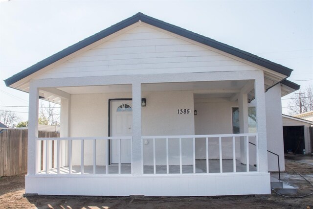 doorway to property with fence, a porch, and stucco siding