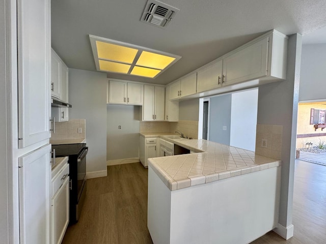 kitchen featuring black electric range, dark wood-style flooring, visible vents, decorative backsplash, and under cabinet range hood