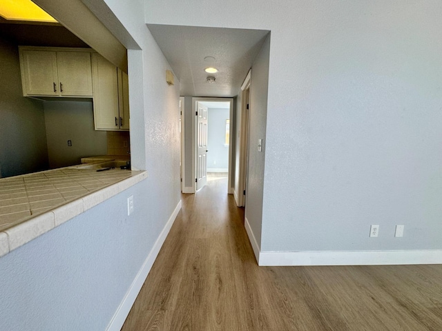 corridor featuring a textured ceiling, wood finished floors, and baseboards