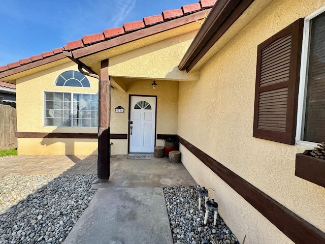 property entrance with a tiled roof, fence, and stucco siding