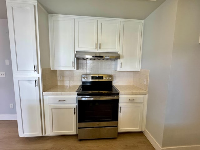 kitchen featuring white cabinets, tile counters, stainless steel range with electric stovetop, and under cabinet range hood