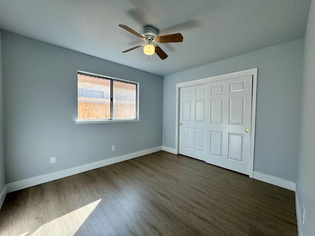 unfurnished bedroom with a closet, dark wood-style flooring, baseboards, and a ceiling fan