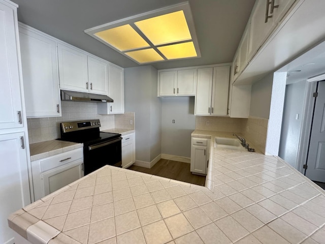 kitchen with range with electric cooktop, backsplash, under cabinet range hood, and tile countertops