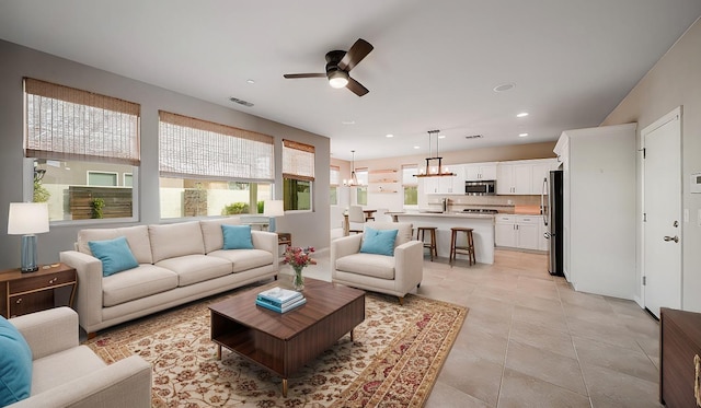 living area featuring ceiling fan with notable chandelier, recessed lighting, visible vents, and light tile patterned floors