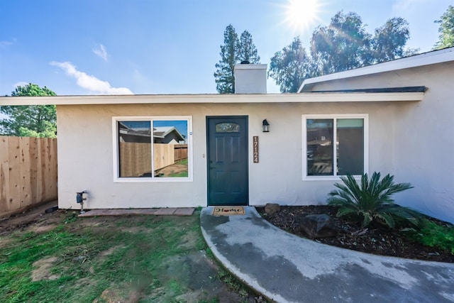 doorway to property with a chimney, fence, and stucco siding