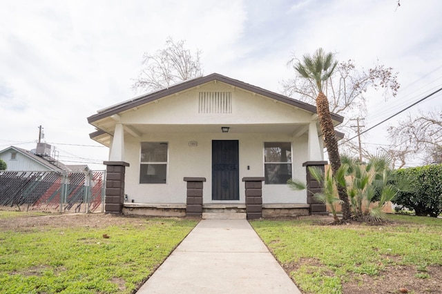 bungalow-style house featuring a front yard, covered porch, fence, and stucco siding