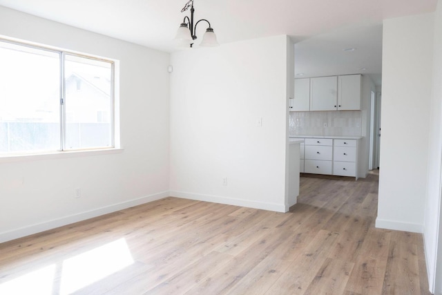 unfurnished dining area with light wood finished floors, baseboards, and an inviting chandelier