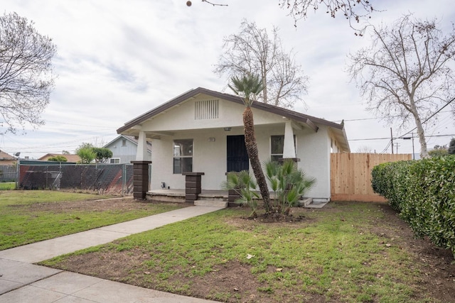 bungalow-style home featuring a porch, a front yard, fence, and stucco siding