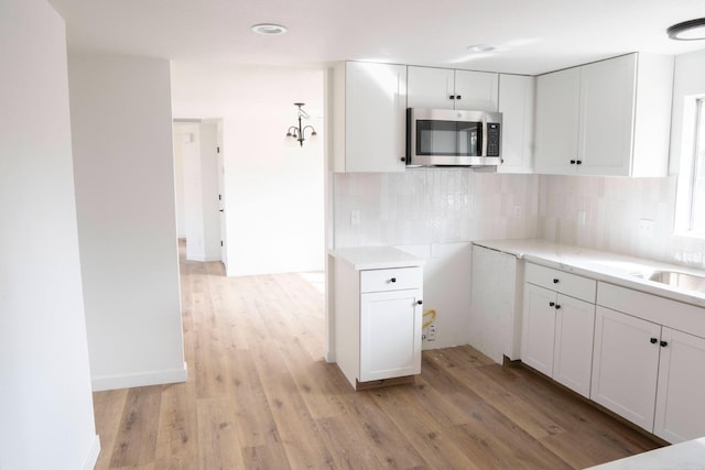 kitchen with light wood-style flooring, white cabinetry, light countertops, decorative backsplash, and stainless steel microwave