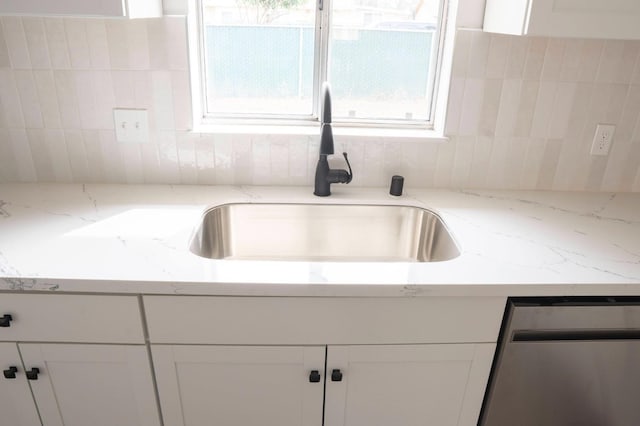 kitchen with light stone countertops, dishwasher, white cabinets, and a sink