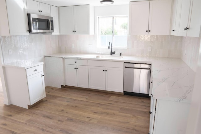 kitchen with white cabinets, appliances with stainless steel finishes, light stone counters, light wood-type flooring, and a sink