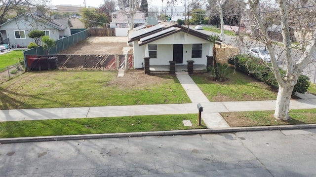 bungalow with fence private yard, solar panels, a front lawn, and stucco siding