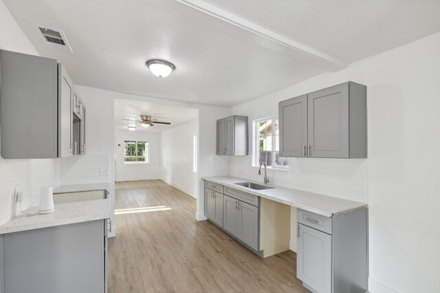 kitchen featuring gray cabinets, visible vents, backsplash, a sink, and light wood-type flooring