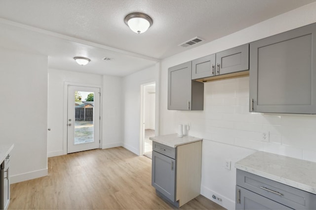 kitchen featuring tasteful backsplash, light wood-type flooring, light stone counters, and gray cabinetry