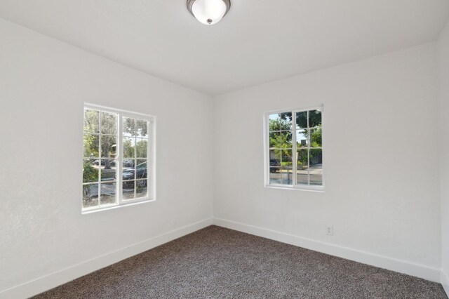 spare room featuring baseboards and dark colored carpet