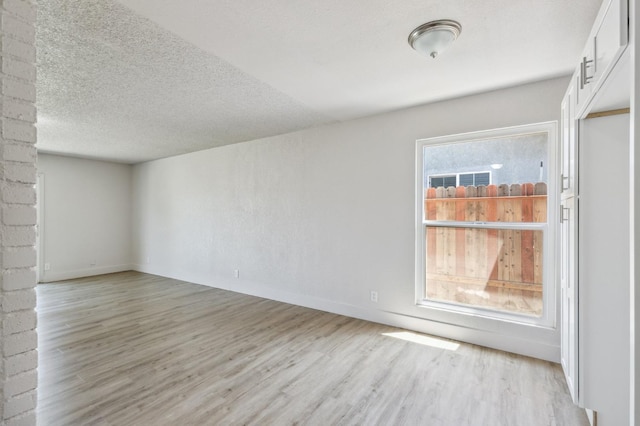 spare room featuring a textured ceiling, light wood finished floors, and baseboards