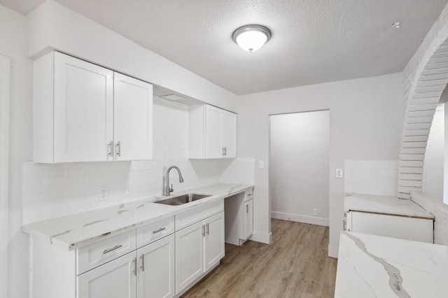 kitchen featuring light stone countertops, white cabinetry, backsplash, and a sink