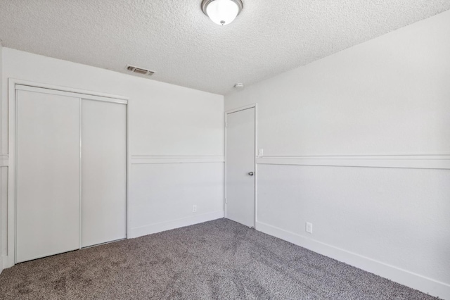 unfurnished bedroom with a textured ceiling, a closet, carpet, and visible vents