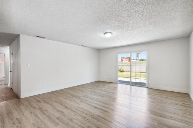 empty room with light wood-type flooring, visible vents, baseboards, and a textured ceiling