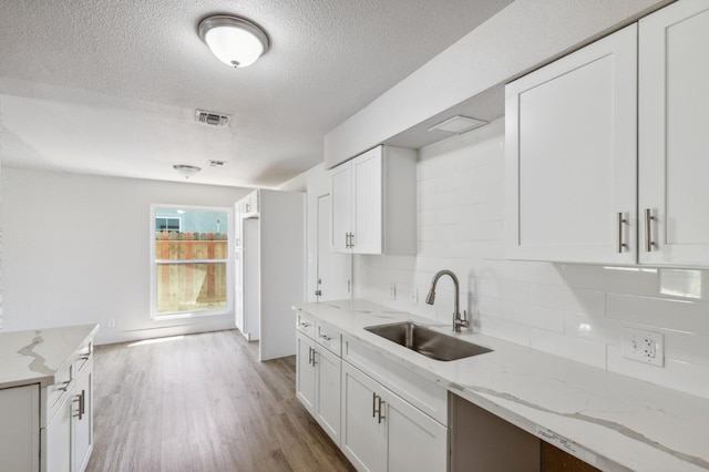 kitchen with white cabinets, visible vents, backsplash, and a sink