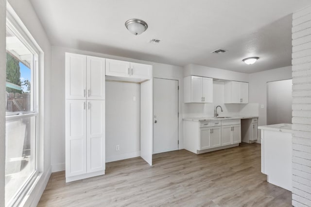 kitchen with light wood-style floors, a sink, visible vents, and white cabinetry