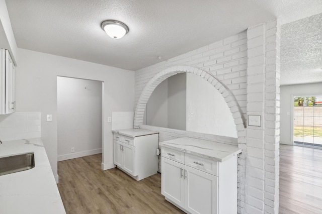 kitchen with light wood finished floors, light stone counters, white cabinets, and a sink