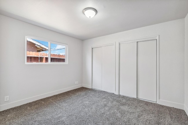 unfurnished bedroom featuring carpet floors, two closets, and baseboards