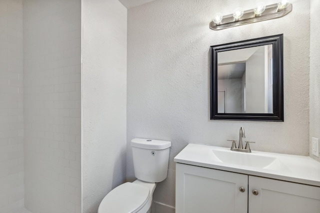 bathroom with a tile shower, a textured wall, vanity, and toilet