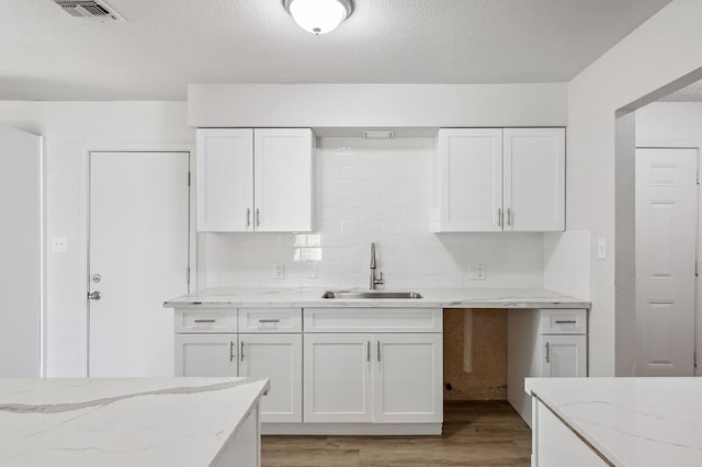 kitchen with visible vents, white cabinets, a sink, light wood-style floors, and backsplash