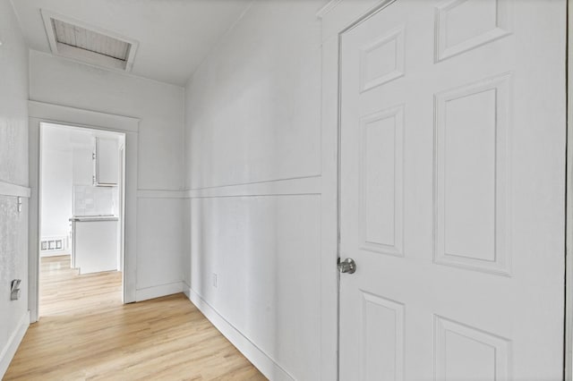 hall featuring attic access, light wood-type flooring, visible vents, and baseboards