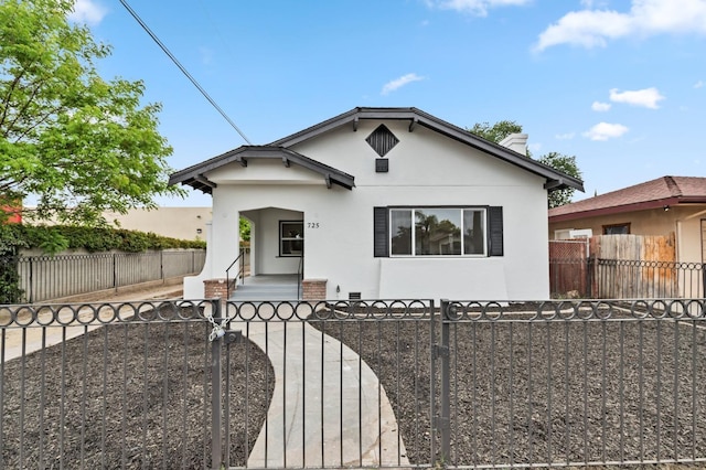 bungalow-style home with a porch, a fenced front yard, a gate, and stucco siding