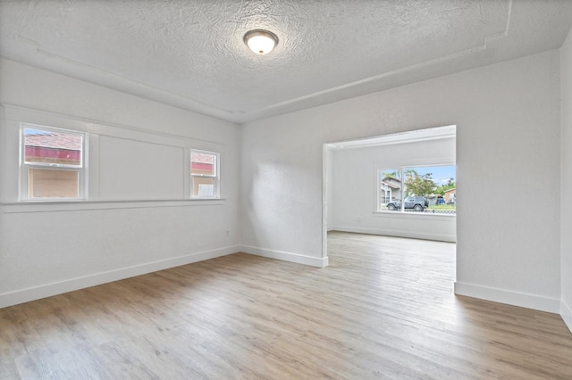 empty room with a textured ceiling, baseboards, and wood finished floors