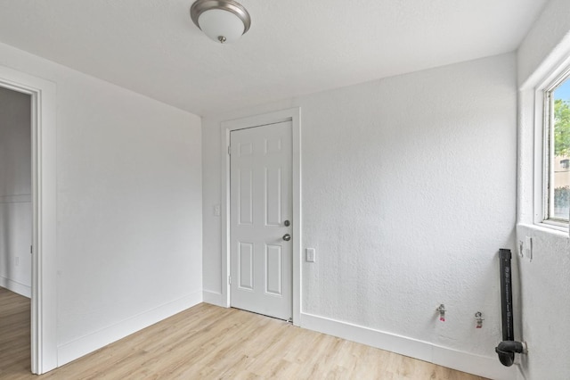 spare room with baseboards, a textured wall, and light wood-style floors