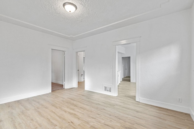 spare room featuring light wood-type flooring, visible vents, a textured ceiling, and baseboards