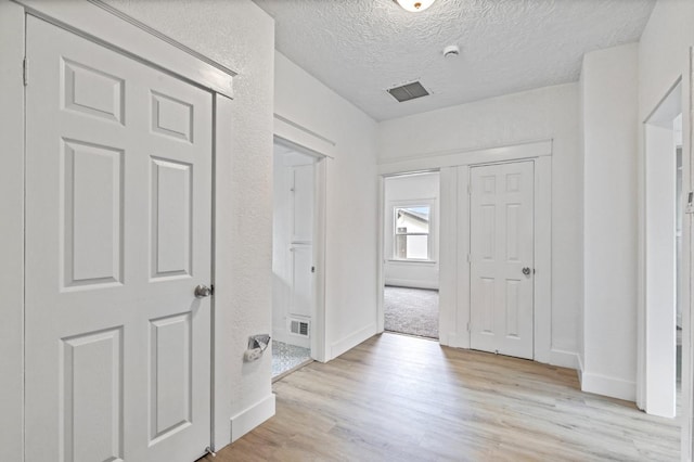 hallway featuring light wood finished floors, baseboards, visible vents, and a textured ceiling