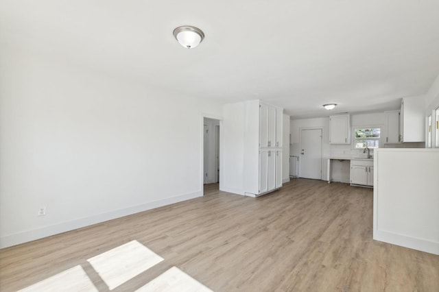 unfurnished living room with light wood-style floors, a sink, and baseboards