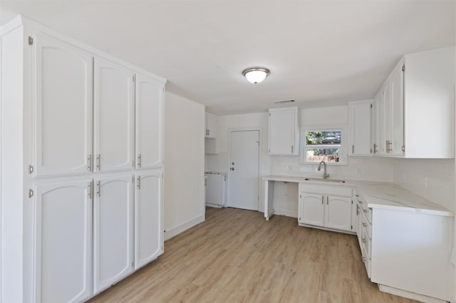 kitchen with visible vents, white cabinets, a sink, light wood-style floors, and backsplash