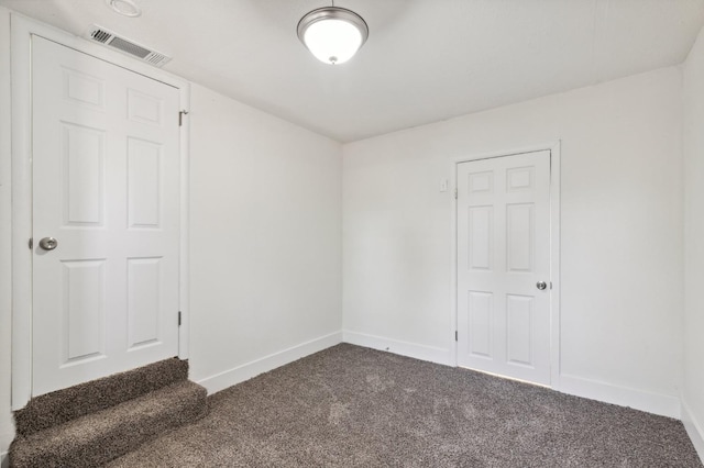 empty room with dark colored carpet, visible vents, and baseboards