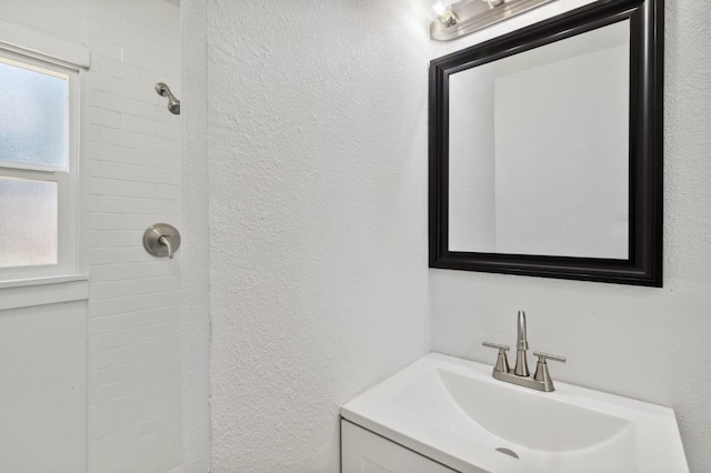 full bath with a textured wall, walk in shower, and vanity