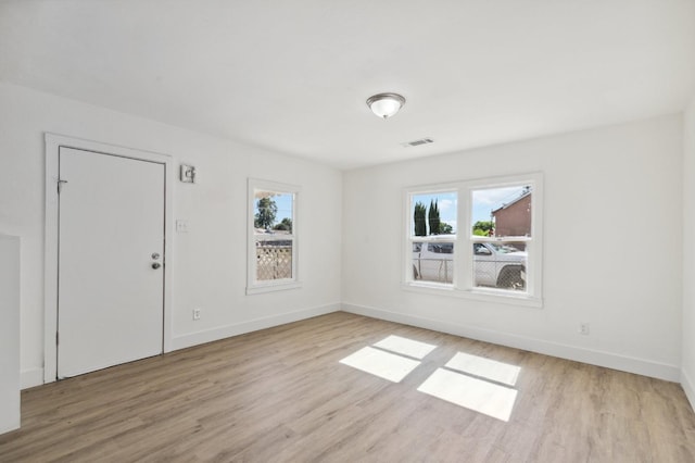 unfurnished room featuring visible vents, light wood-style flooring, and a wealth of natural light