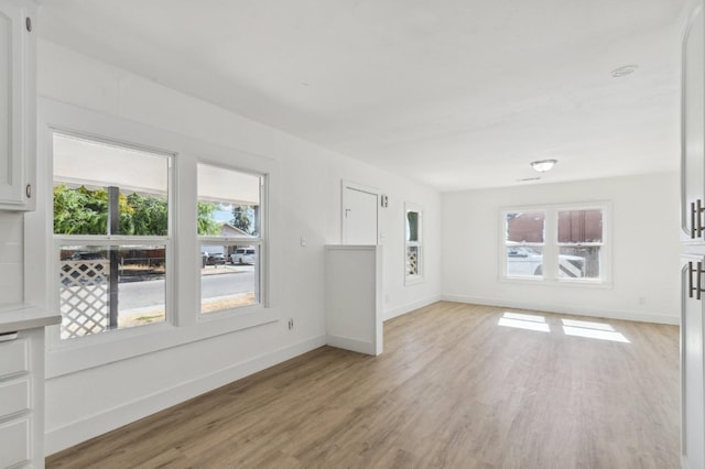 unfurnished living room with light wood finished floors, baseboards, and a wealth of natural light