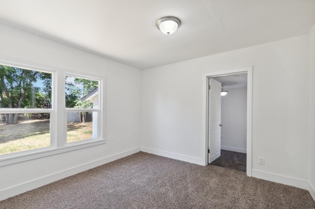 spare room with baseboards and dark carpet