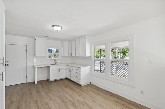 kitchen featuring light wood finished floors, tasteful backsplash, visible vents, light countertops, and white cabinetry