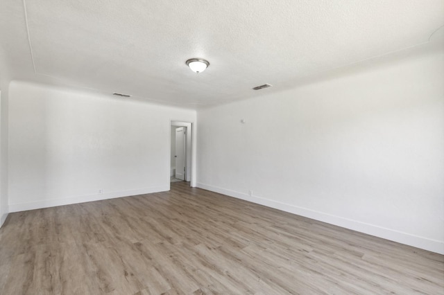 spare room with light wood-style floors, baseboards, visible vents, and a textured ceiling