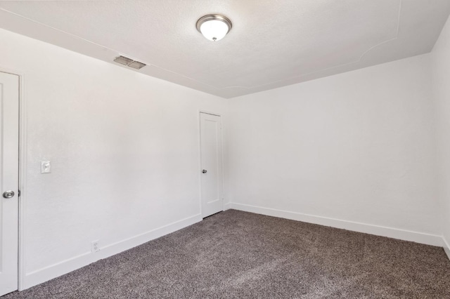 empty room with baseboards, visible vents, dark carpet, and a textured ceiling