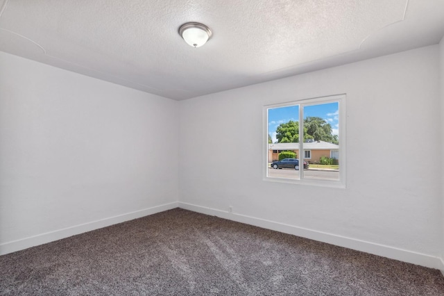 spare room featuring a textured ceiling, dark carpet, and baseboards