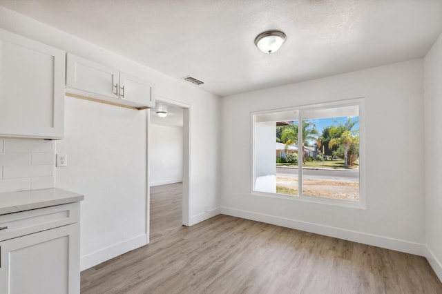 unfurnished dining area featuring light wood-type flooring, visible vents, and baseboards